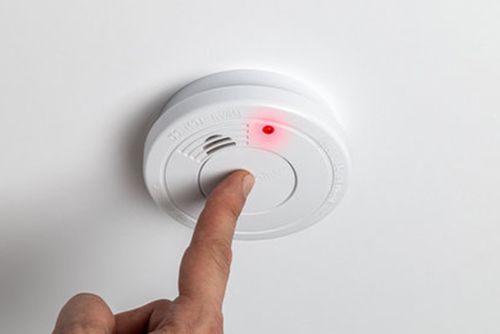 Person testing a ceiling smoke alarm